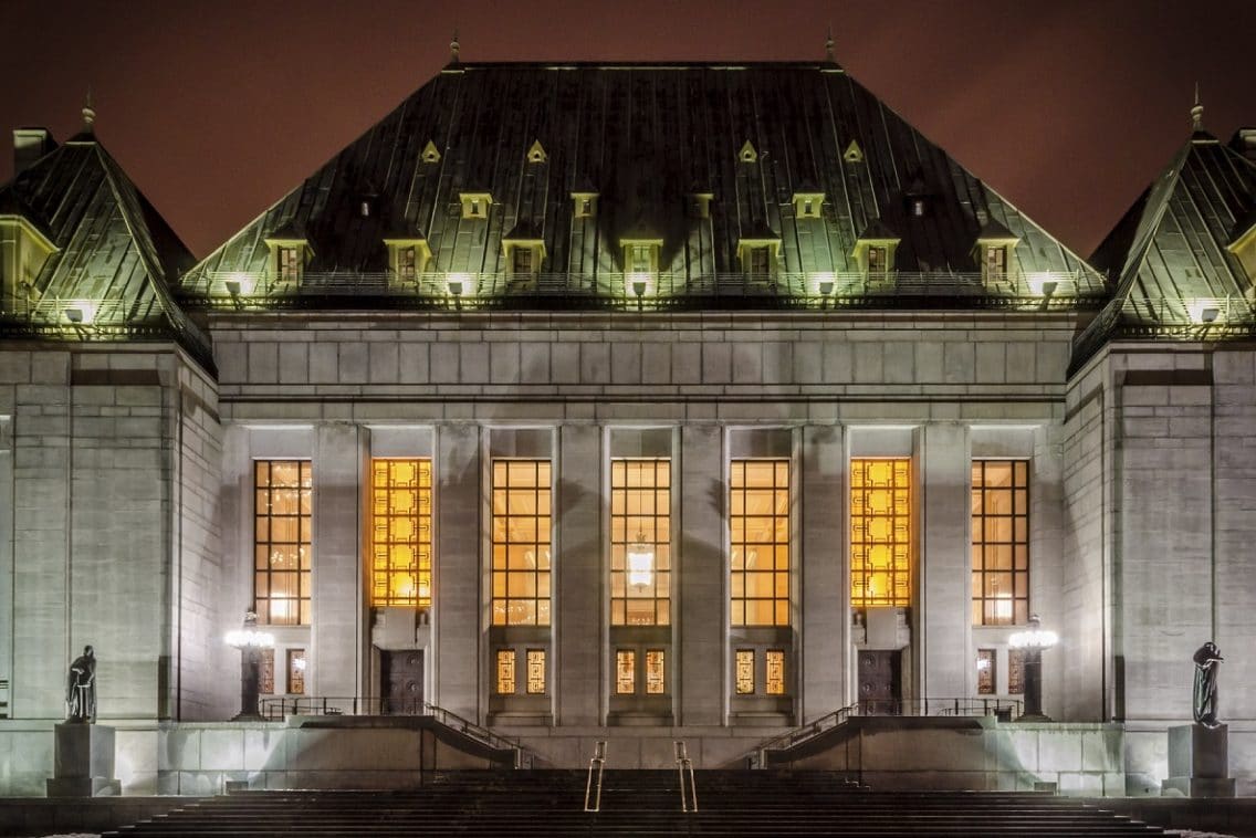 The Supreme Court of Canada building stands lit up at night.
