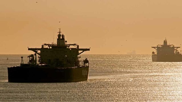 Two oil tankers stand in the still water at sunset.
