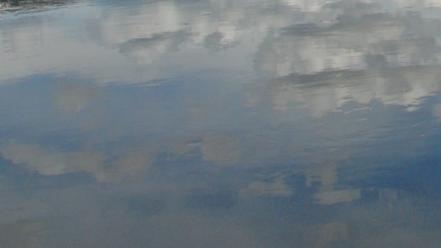 The sky with clouds is reflected in still water.