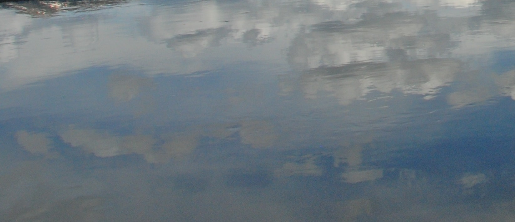 The sky with clouds is reflected in still water.