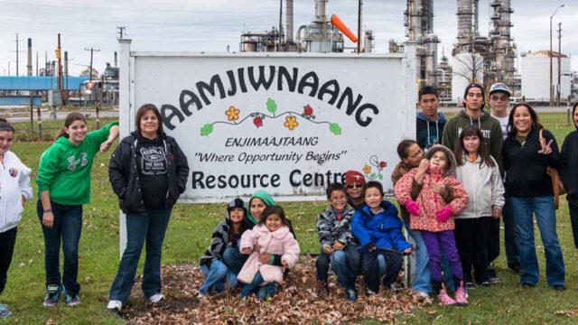 Members of the Aamjiwnaang First Nation stand in front of a sign for a resource centre