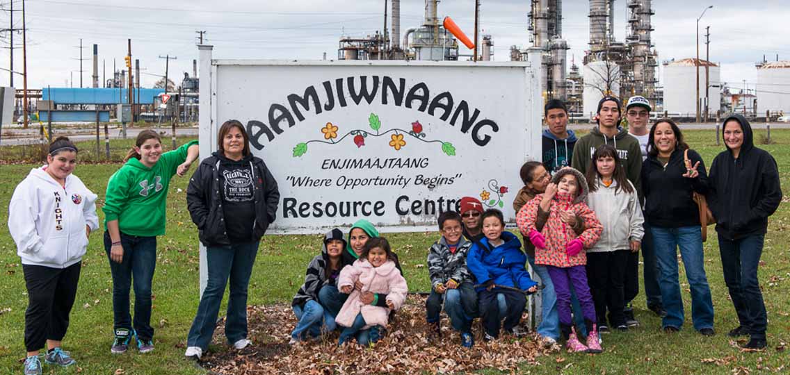 Members of the Aamjiwnaang First Nation stand in front of a sign for a resource centre