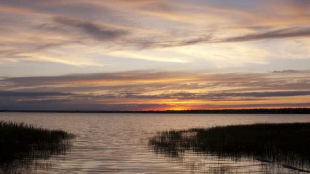 The mouth of a great lake opens into a large body of water at sunset.