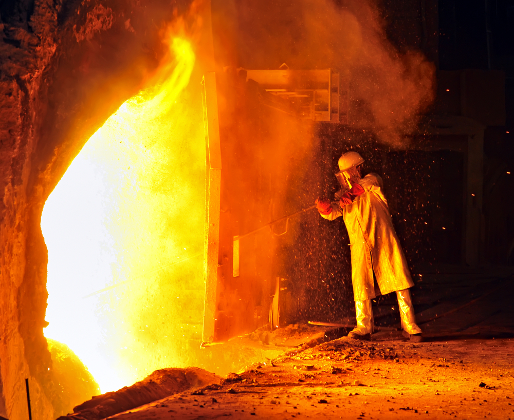 A worker wears protective clothing and works near a large fire.