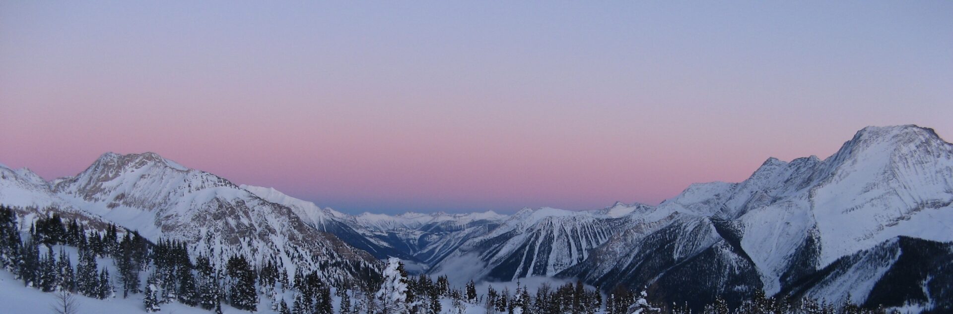 A landscape of large snow covered mountains at dusk.