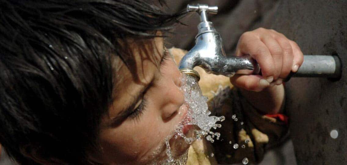 A child drinks water that flows from a silver tap.