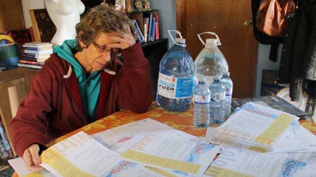 Marlene Brown sits at a table with her hand on her head. Many papers are scattered across a table as she looks them over. Bottles of water are next to her.