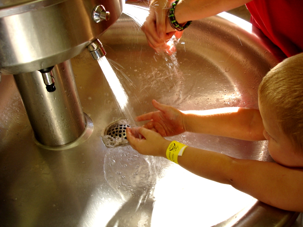 Photo of two children washing hands in a metal sink.