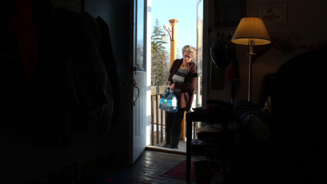 A person walks through the front door of a home carrying large bottles of water.