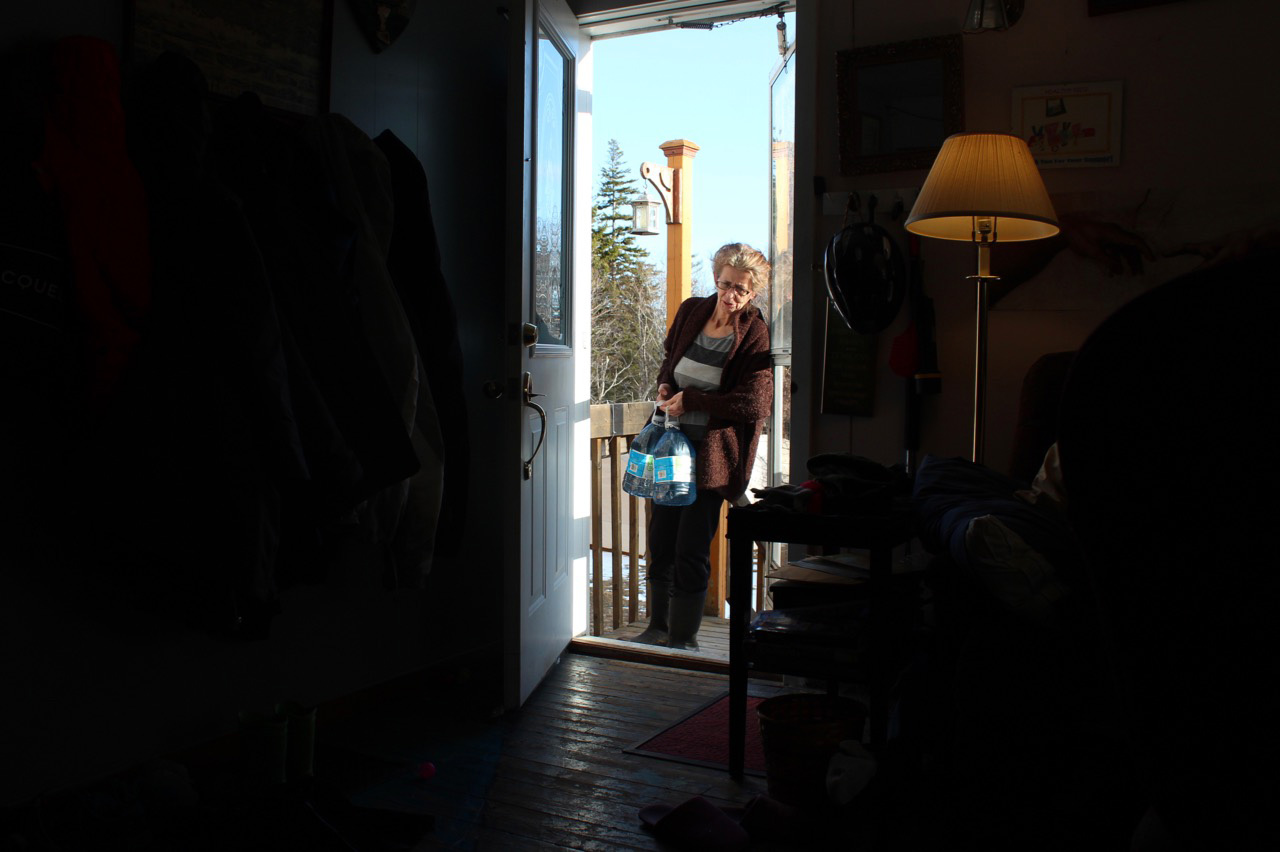 A person walks through the front door of a home carrying large bottles of water.