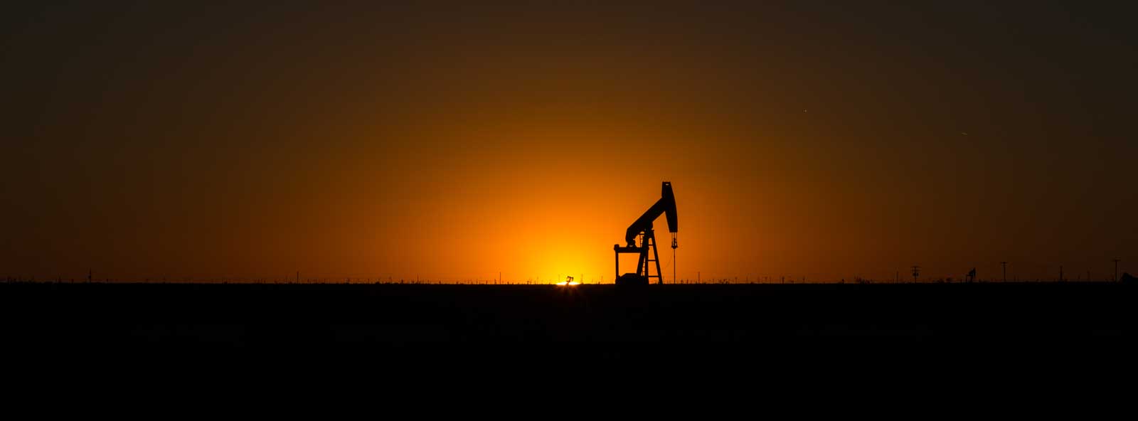 An oil and gas pumpjack against a bright orange sunset