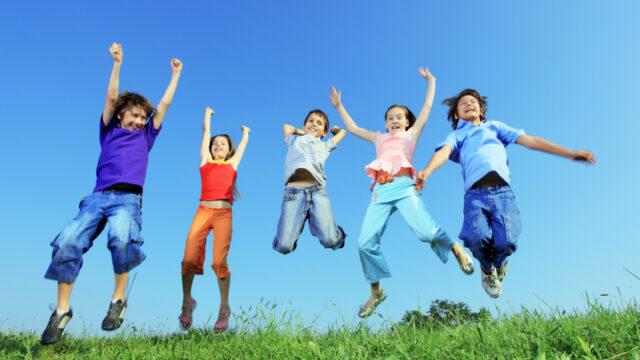 A low angle shows children that jump and raise their arms in celebration.