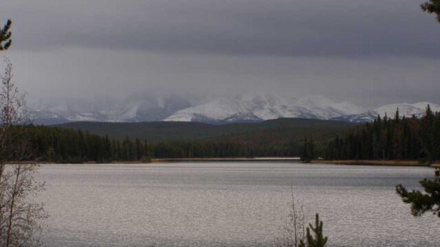 A large lake in the rain. In the distance a snow covered mountain stands concealed by grey clouds.
