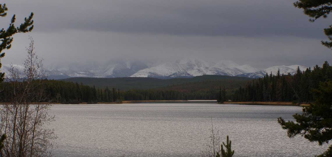 A large lake in the rain. In the distance a snow covered mountain stands concealed by grey clouds.