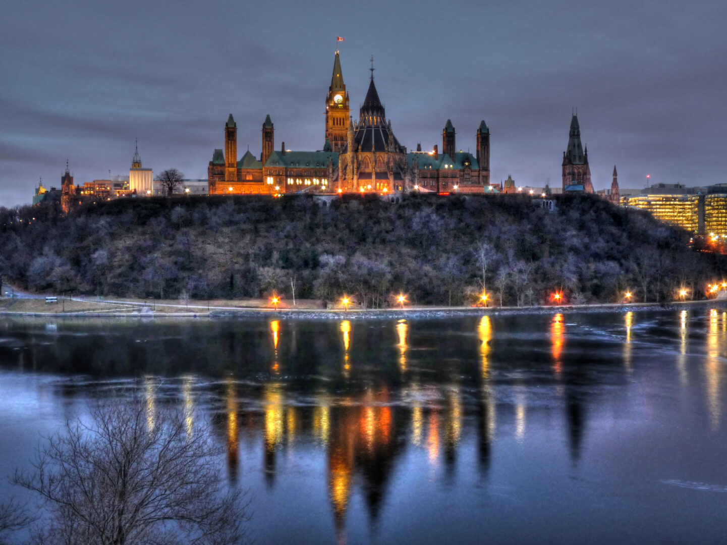Parliament Hill is lit up at dusk. The water around reflects the building's lights.