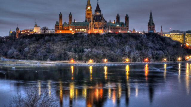Parliament Hill is lit up at dusk. The water around reflects the building's lights.