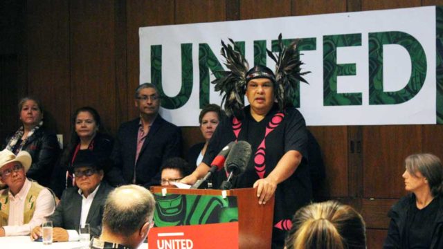 Sundance Chief Rueben George speaks at a press conference. He wears a traditional headdress.