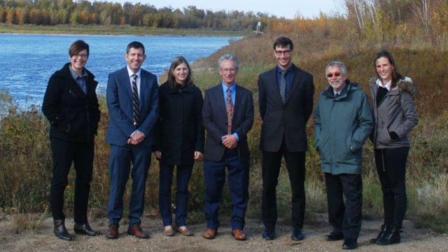 A group of lawyers stand outside in the grass near a small lake.