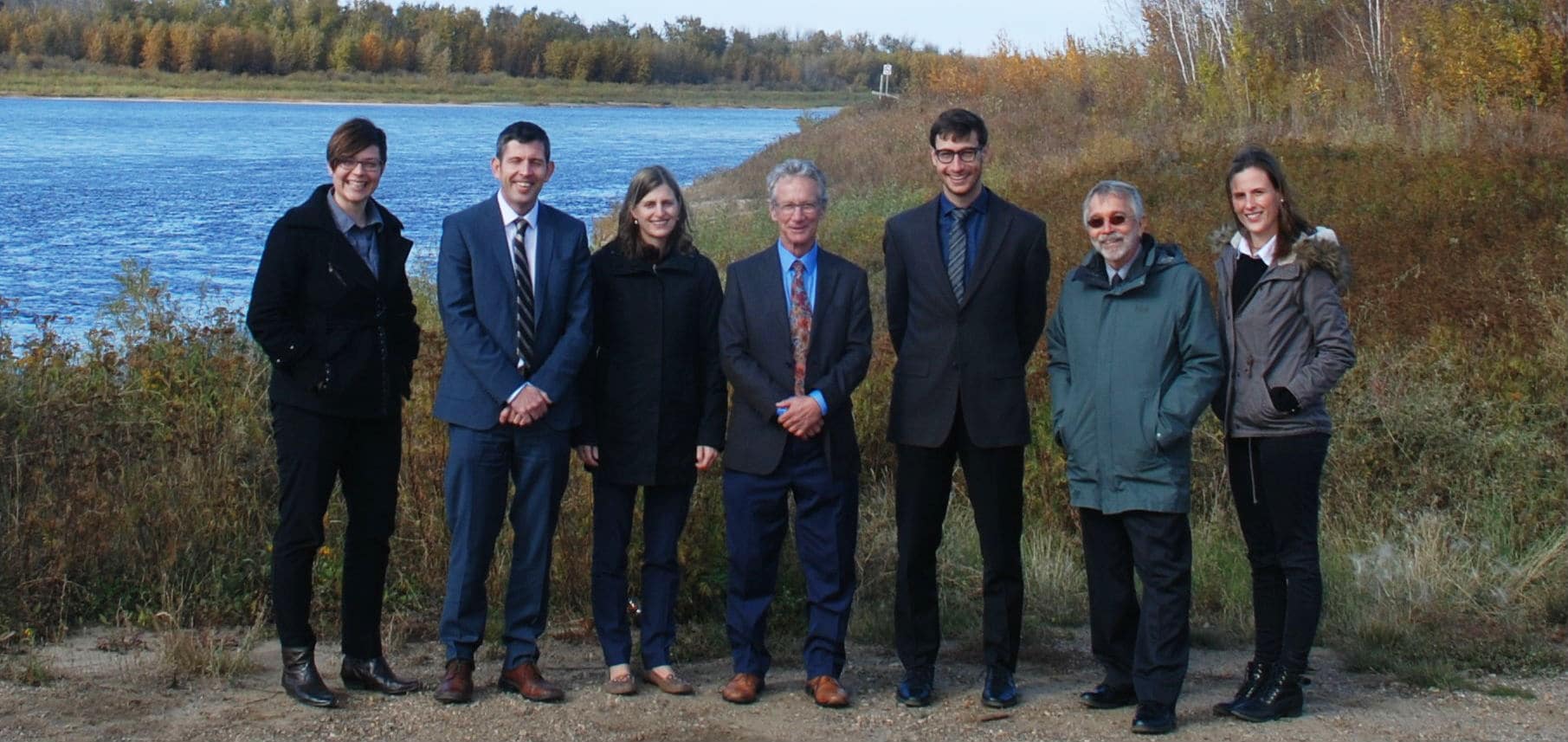 A group of lawyers stand outside in the grass near a small lake.
