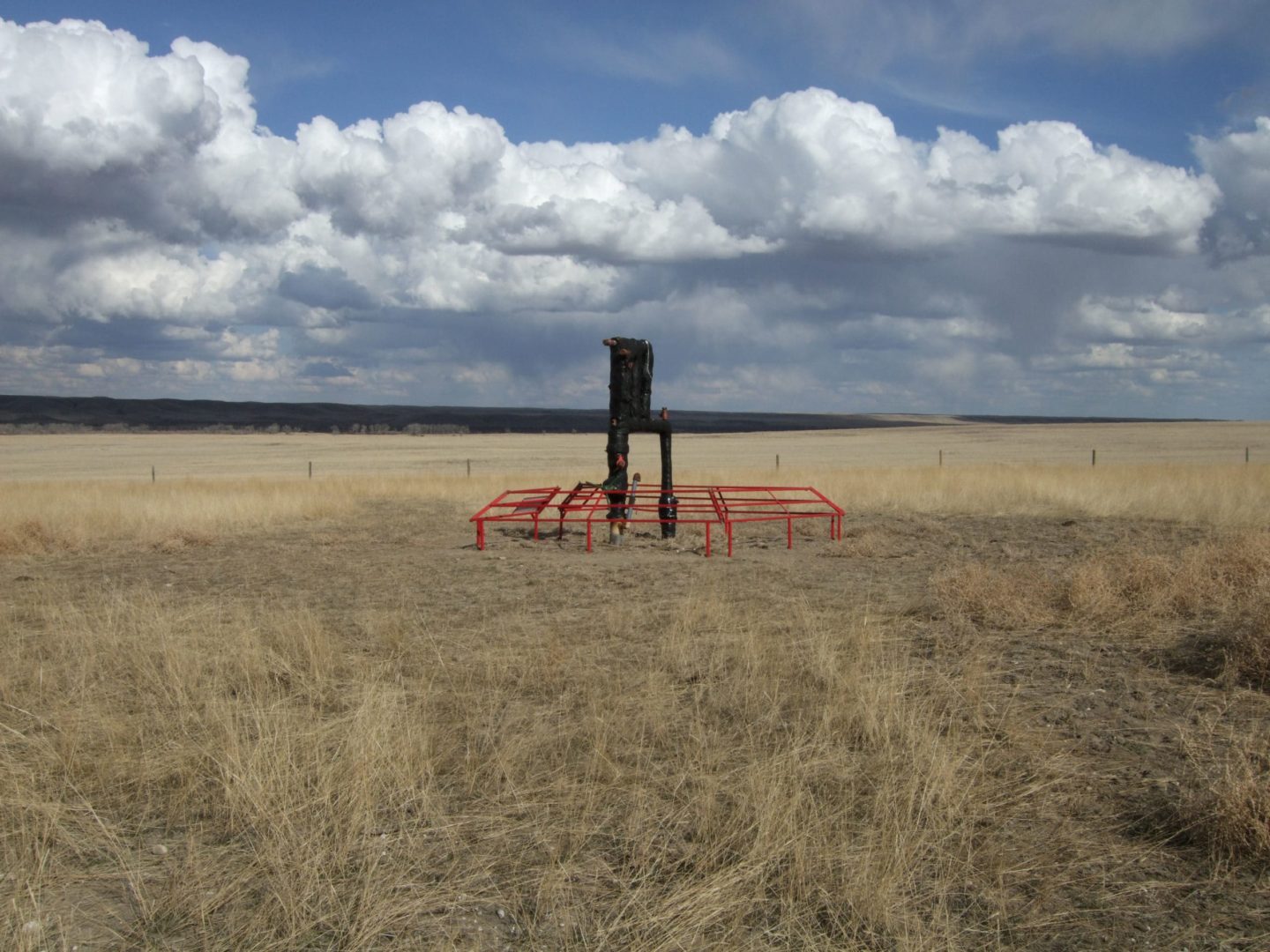 A gas well sits in the middle of a flat field. White clouds are in the sky.