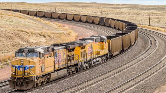 A long coal train comes around a corner on a track.