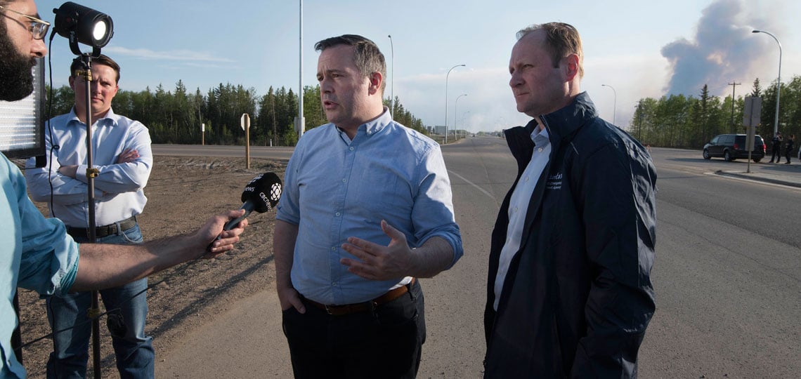 Jason Kenney stands in front of a wildfire
