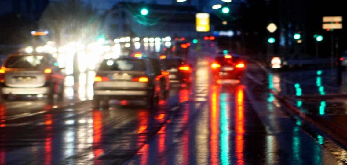 Blurry traffic on a road filled with cars at night. The street lights and car lights reflect on the wet black pavement.