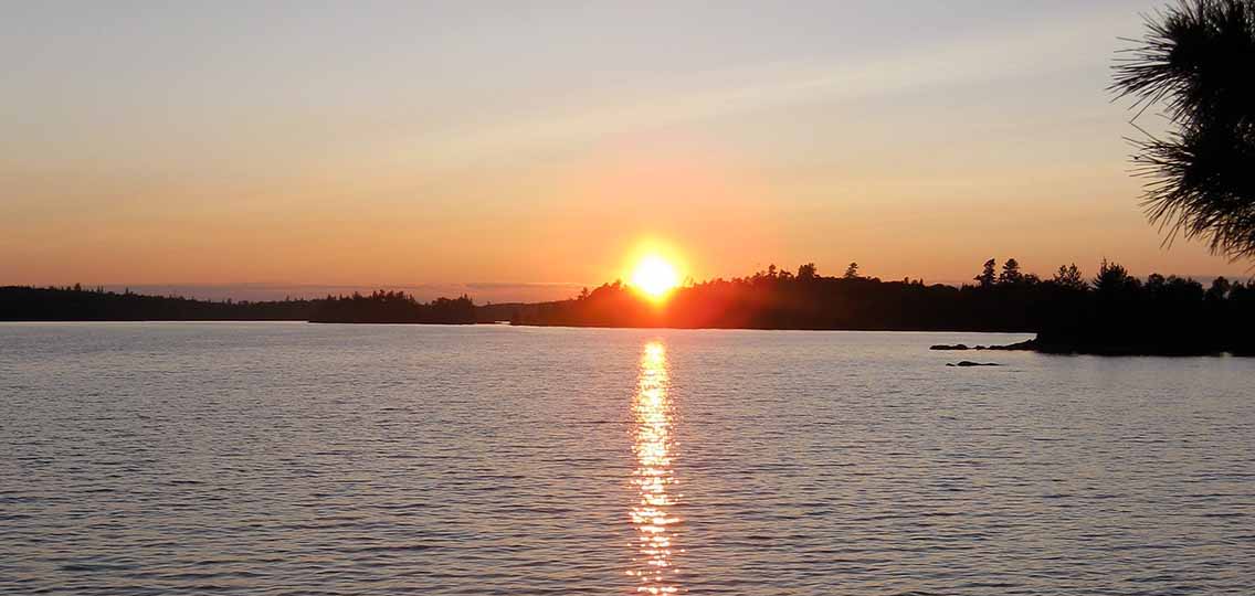 a large lake reflects an orange sunset.