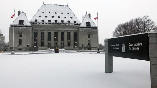 The Supreme Court of Canada building has snow on its roof and snow covers the ground nearby.