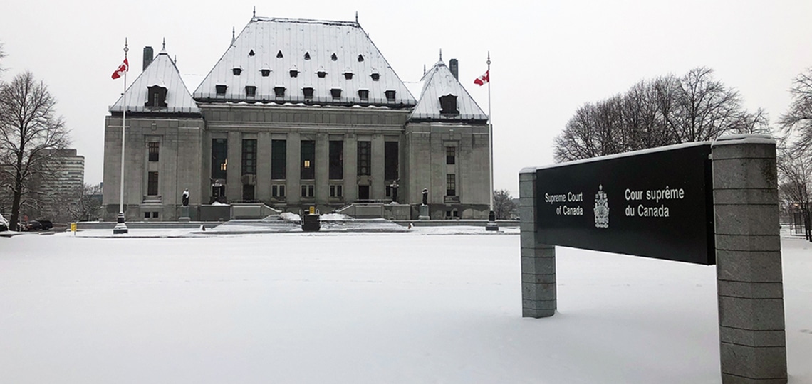 The Supreme Court of Canada building has snow on its roof and snow covers the ground nearby.