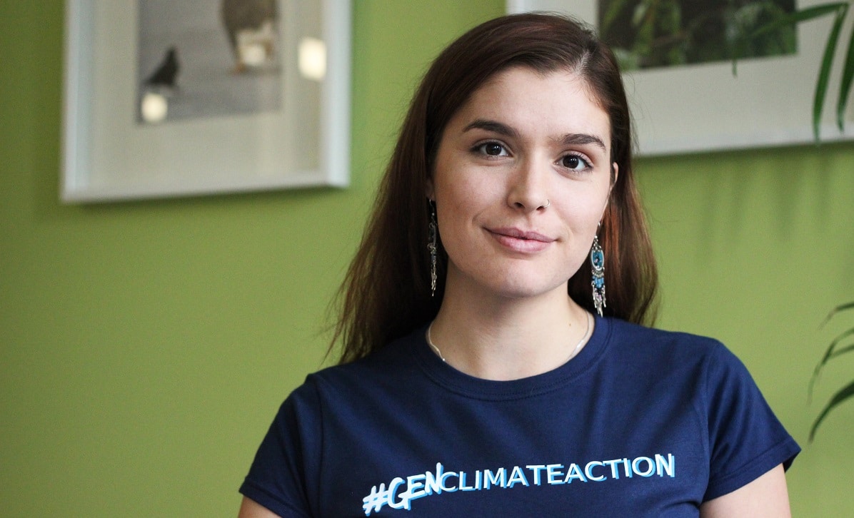 Shaelyn smiles and wears a hashtag gen climate action t-shirt. She has long brown hair.