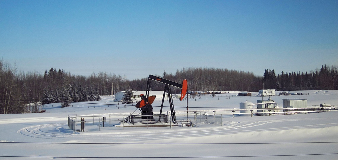 Oil wells stand in the snow of a flat field.