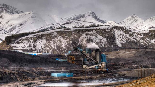 A coal mine stands on flat, wet ground. In the distance are snow capped mountains.