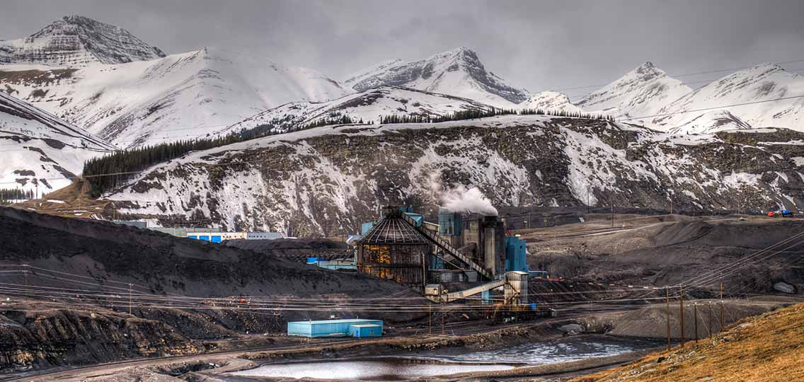 A coal mine stands on flat, wet ground. In the distance are snow capped mountains.