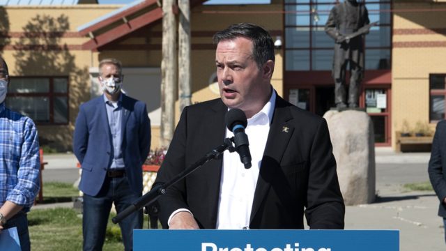 Alberta Premier Jason Kenney stands outside and speaks into a microphone.