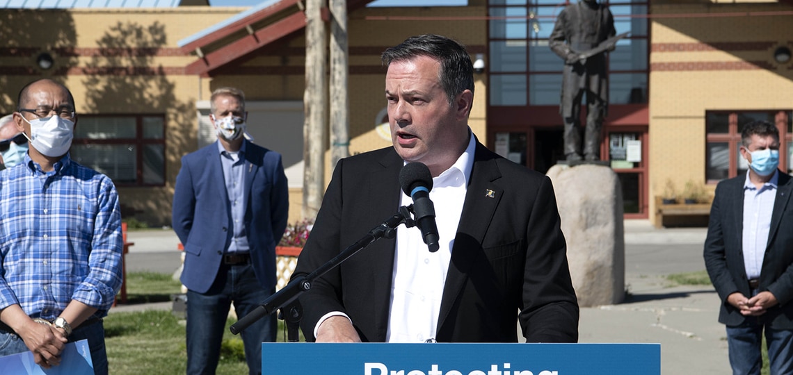 Alberta Premier Jason Kenney stands outside and speaks into a microphone.