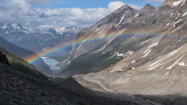 A rainbow arches across two rocky mountains.