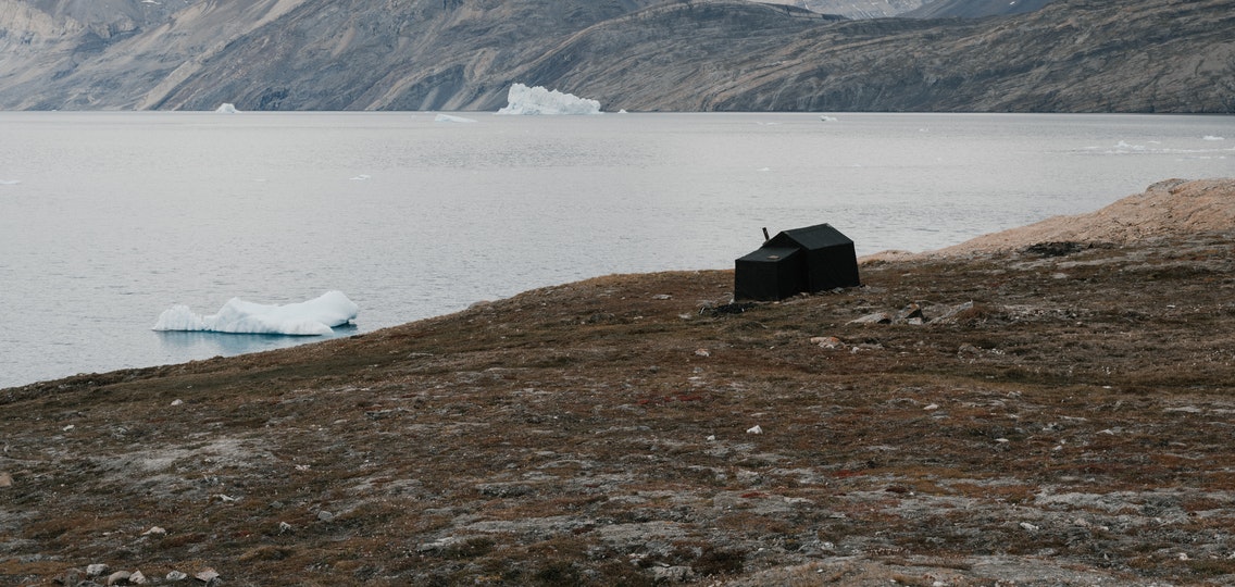 A small shack on the rocky shoreline of icy water.