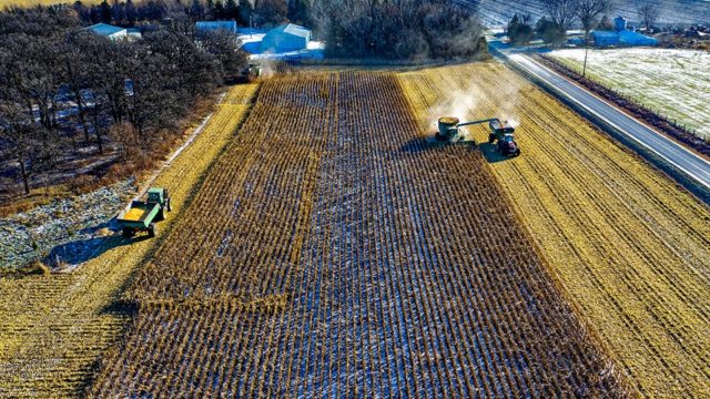 An aerial view of farmland. Two tractors harvest crops in the field.