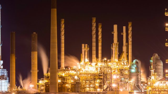 An oil refinery with many smoke stacks is lit up at night.
