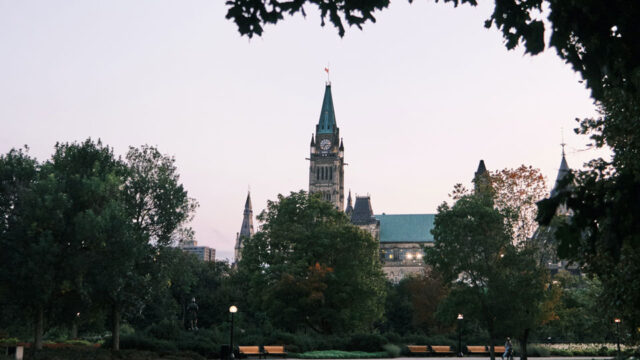 A Canadian Parliament building stands in the distance behind trees in the park.