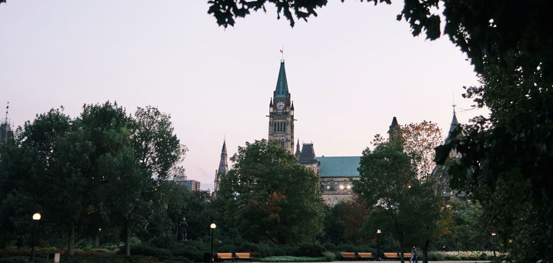 A Canadian Parliament building stands in the distance behind trees in the park.