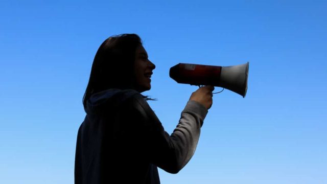 A woman holds a megaphone against the background of a blue sky.