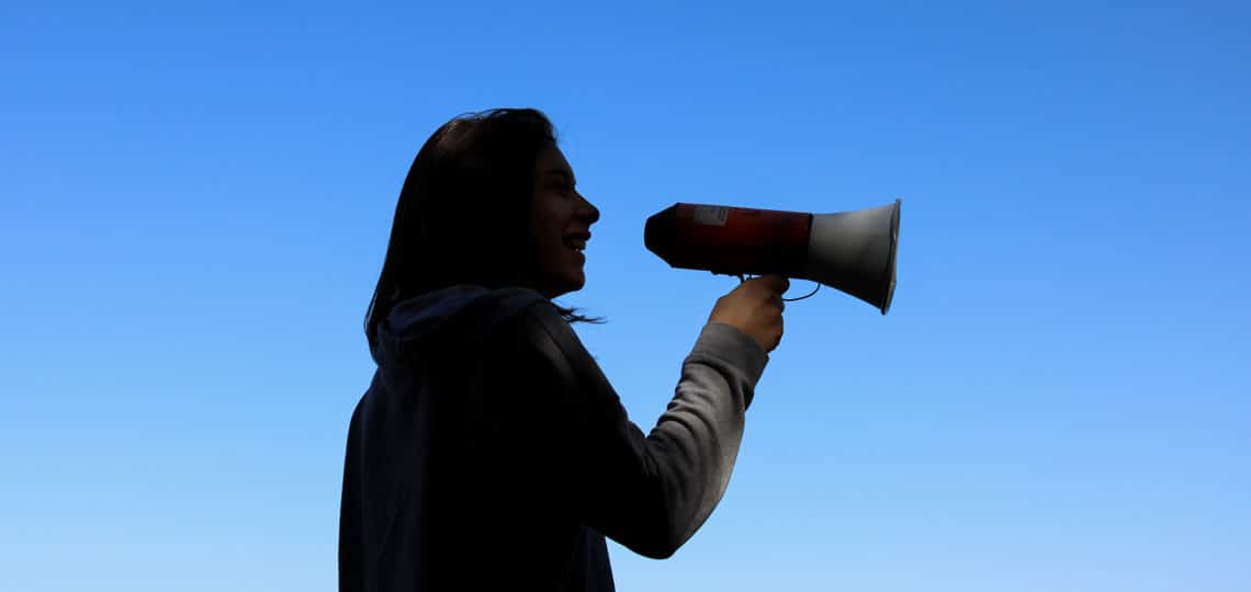 A woman holds a megaphone against the background of a blue sky.