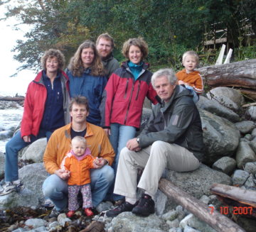 A team family photo where 6 adults and 2 children stand and sit on rocks outside. They all wear jackets.