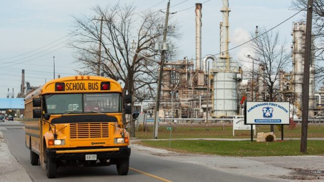 A school bus drives past an oil refinery.