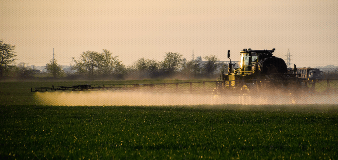 A large tractor sprays pesticides on a field of crops.