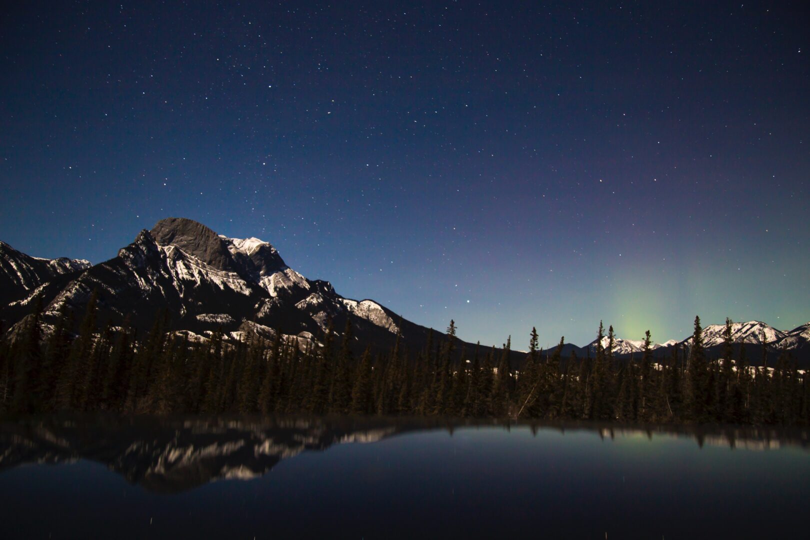 A starry night over a snow-capped mountain and alpine lake in Alberta.