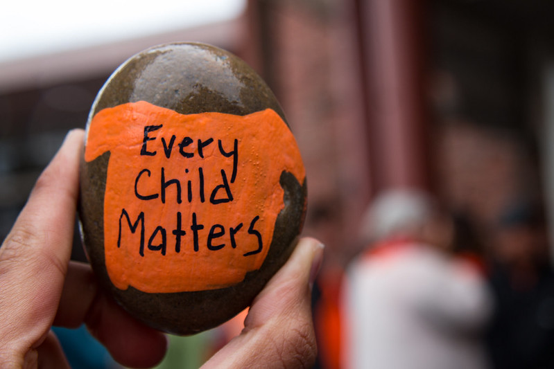 Hand holding rock painted with orange Every Child Matters tshirt