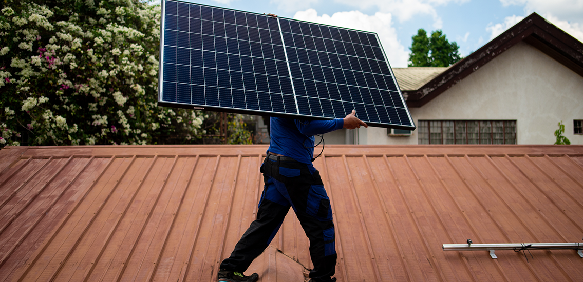 Worker carrying a solar panel across a rooftop